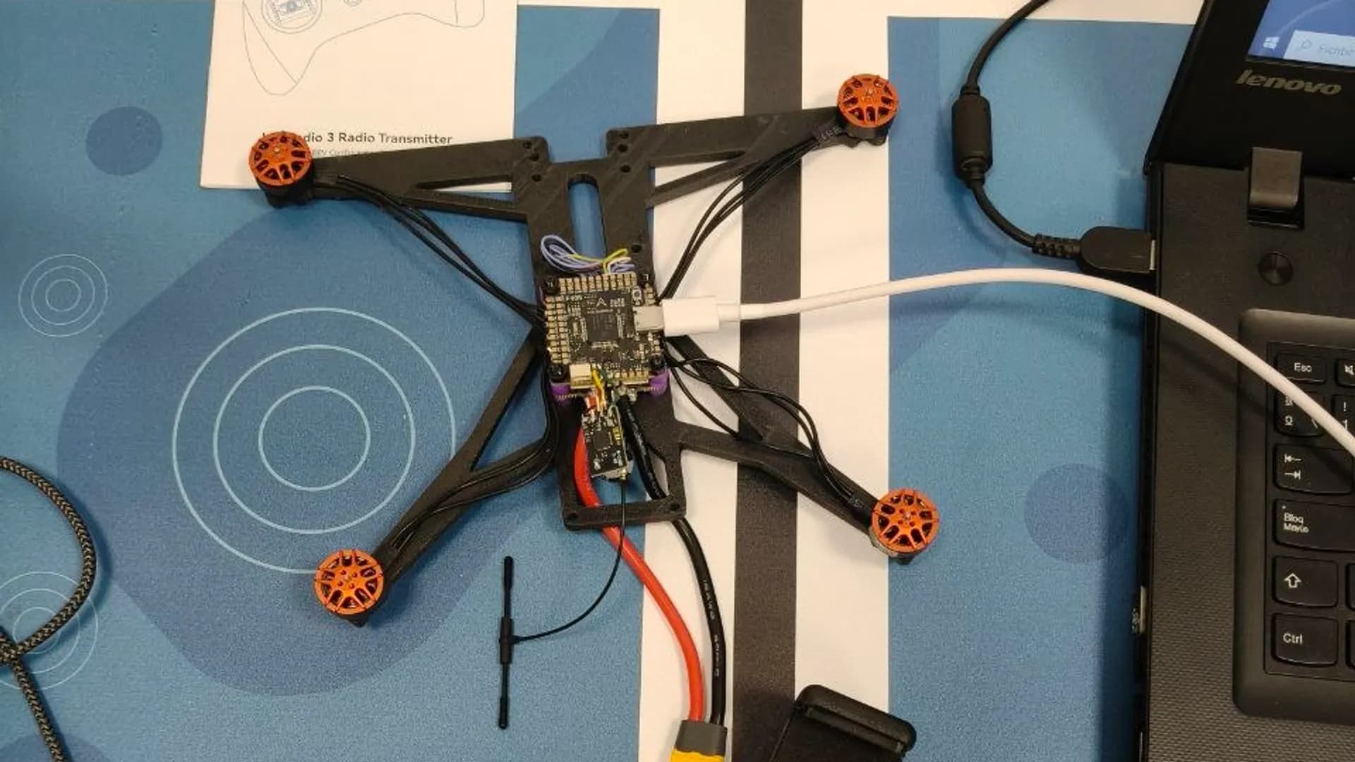 Chasis de un dron FPV a medio montar, con la controladora de vuelo cableada y la emisora al lado