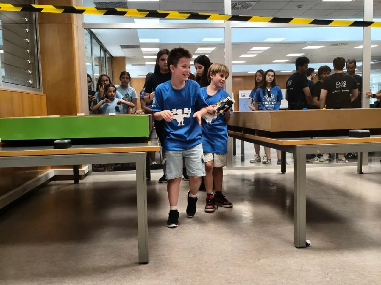 Dos miembros del Club cruzando la sala con su robot en una jornada de competición
